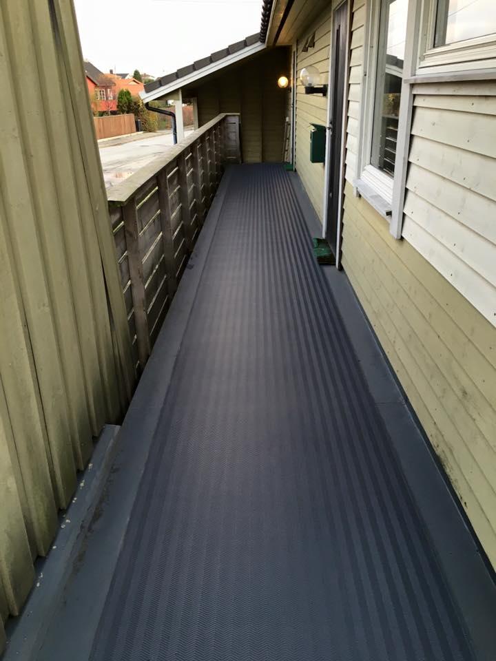 A long balcony walkway along a house, sealed with dark membrane