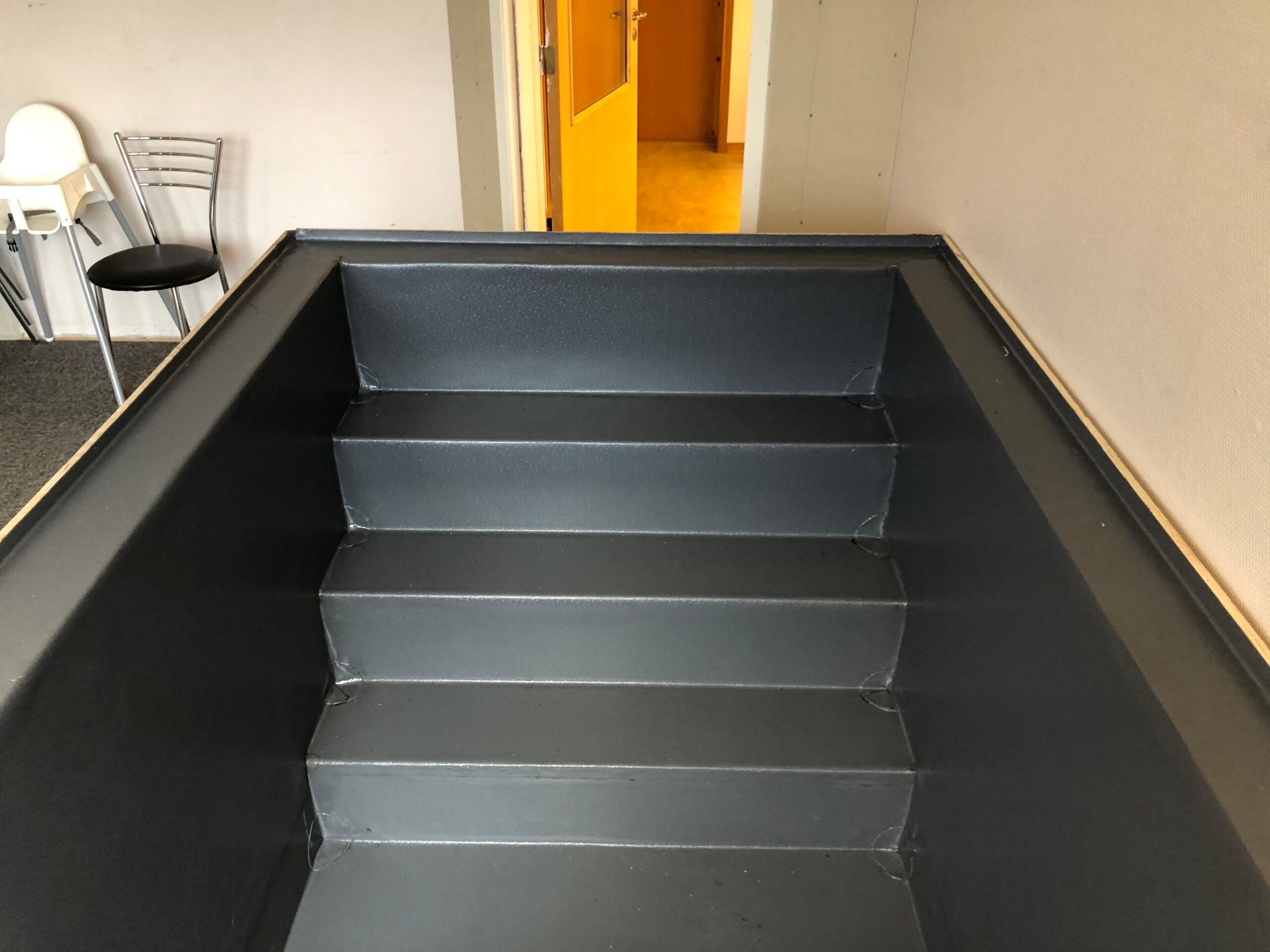 A baptismal font lined with grey membrane, with steps down into it