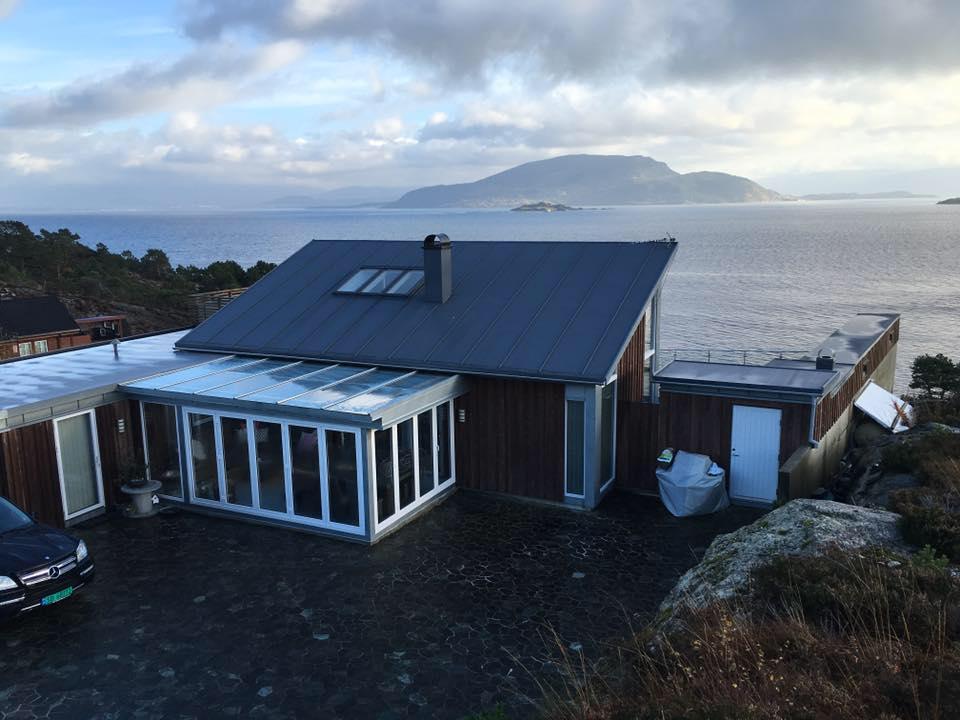 A house by the sea with a dark metal roof and a glass extension